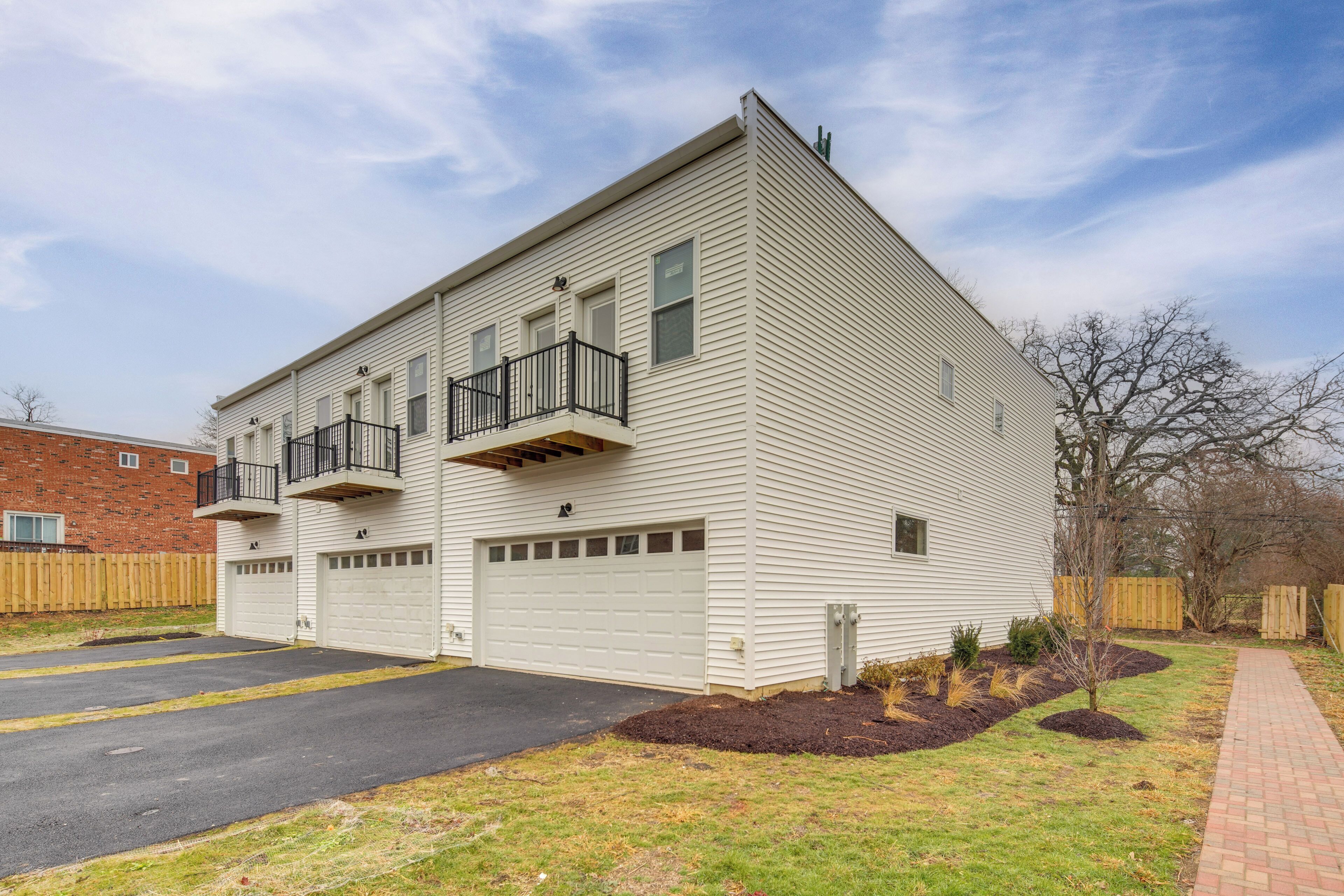 A two-story building with a garage, a balcony, and a brick wall in the background.