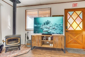 Un salón con estufa de leña, televisor sobre un mueble de madera y una puerta con señal de salida.