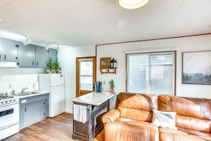 Un espacio habitable compacto con kitchenette, un sofá de cuero marrón y una ventana con persianas.