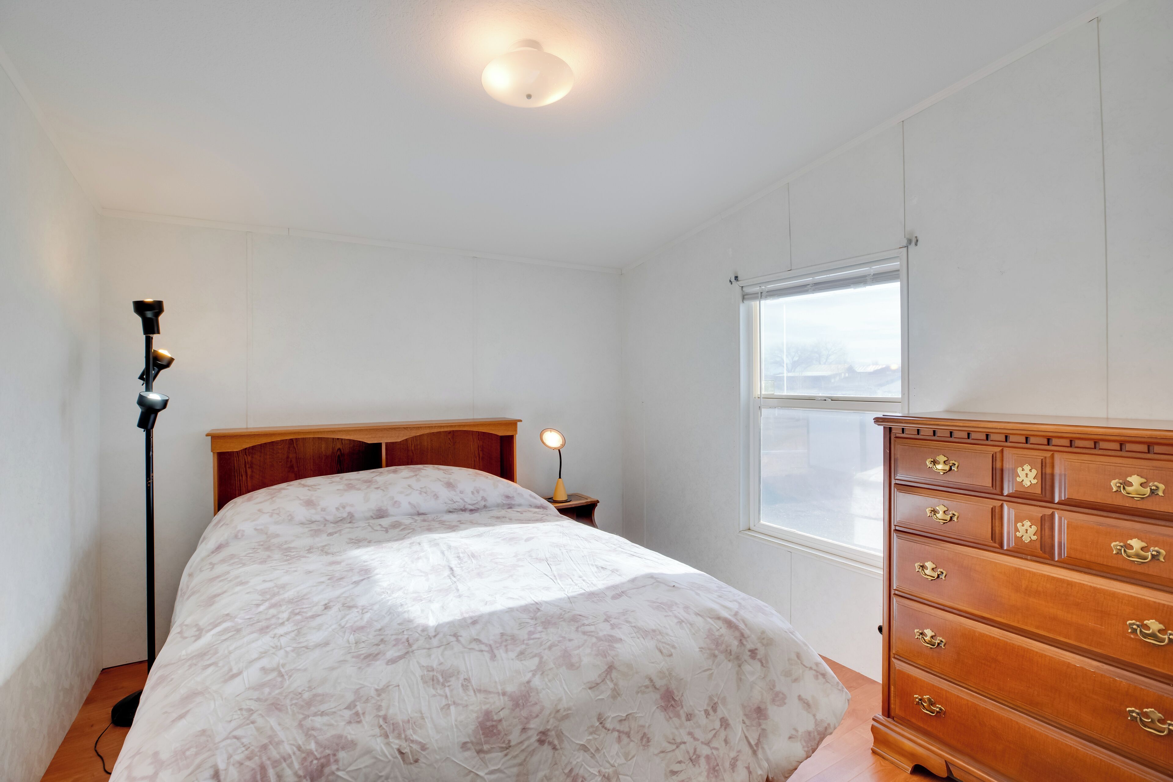 A bedroom with a bed, dresser, nightstand, lamp, and window.