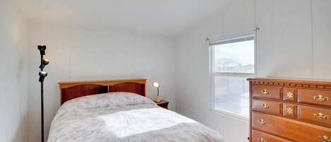 A bedroom with a bed, dresser, nightstand, lamp, and window.