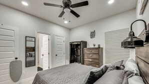 Een slaapkamer met een bed, een dressoir, een kledingkast, een plafondventilator en wanddecoratie.