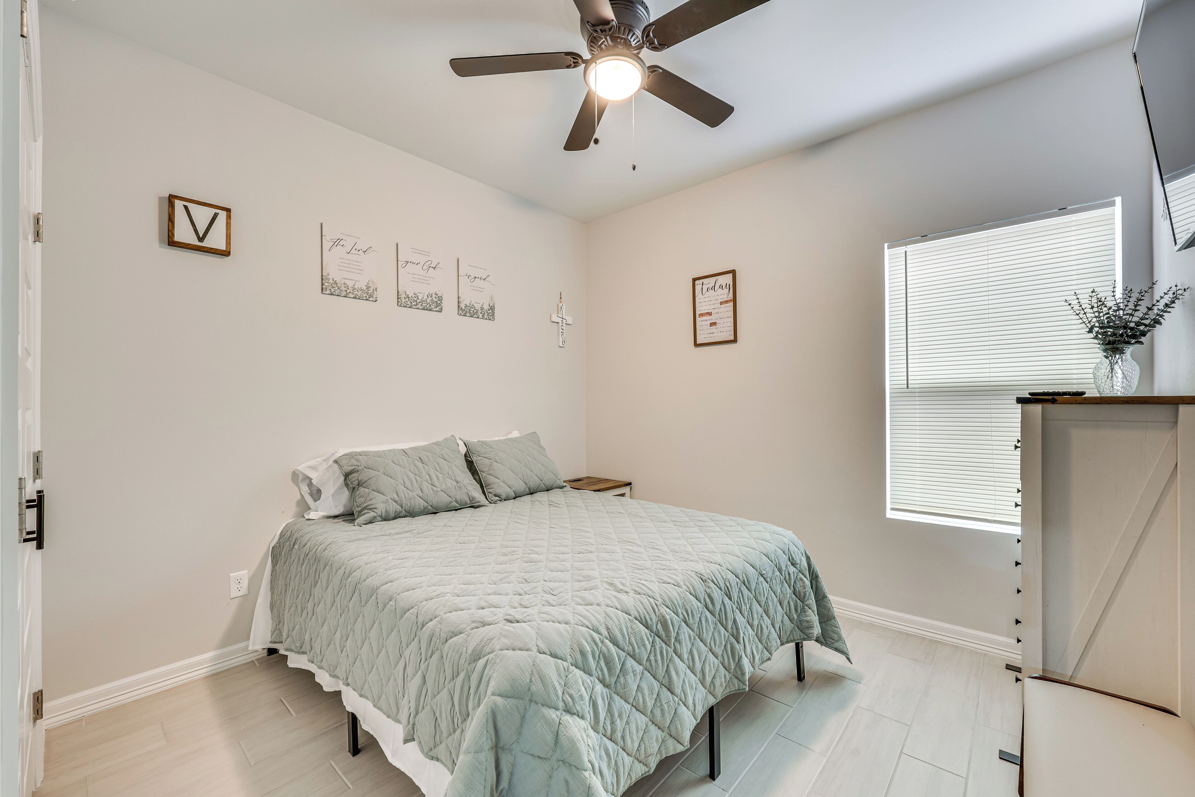 A bedroom with a bed, a ceiling fan, a window with blinds, and wall decorations.