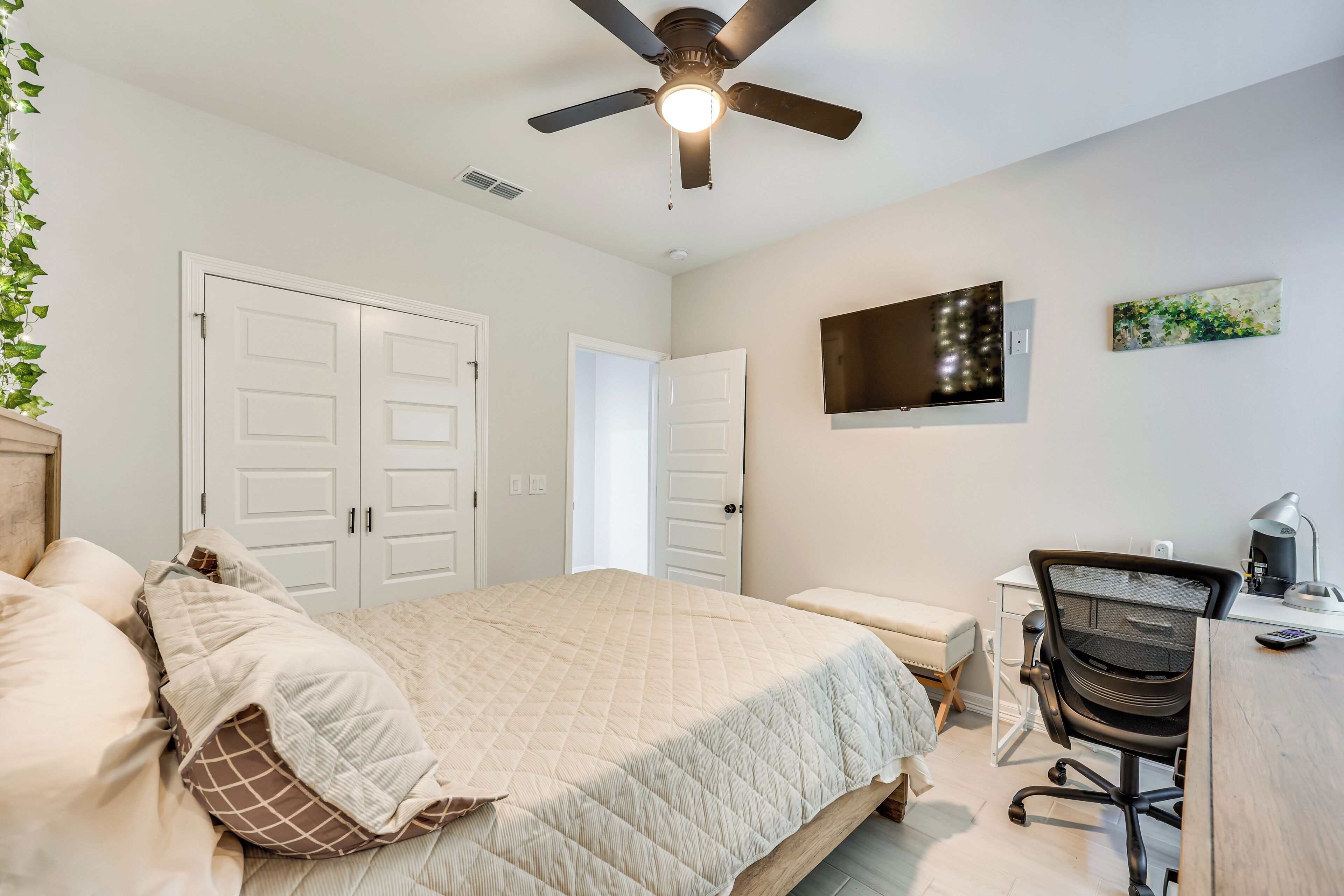 Une chambre à coucher avec un lit, un bureau, une chaise, un ventilateur de plafond et un téléviseur fixé au mur.