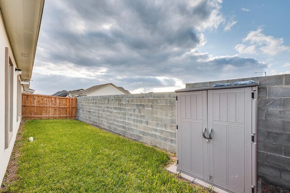 A backyard with a grassy lawn, a wooden fence, a stone wall, and a metal utility shed.