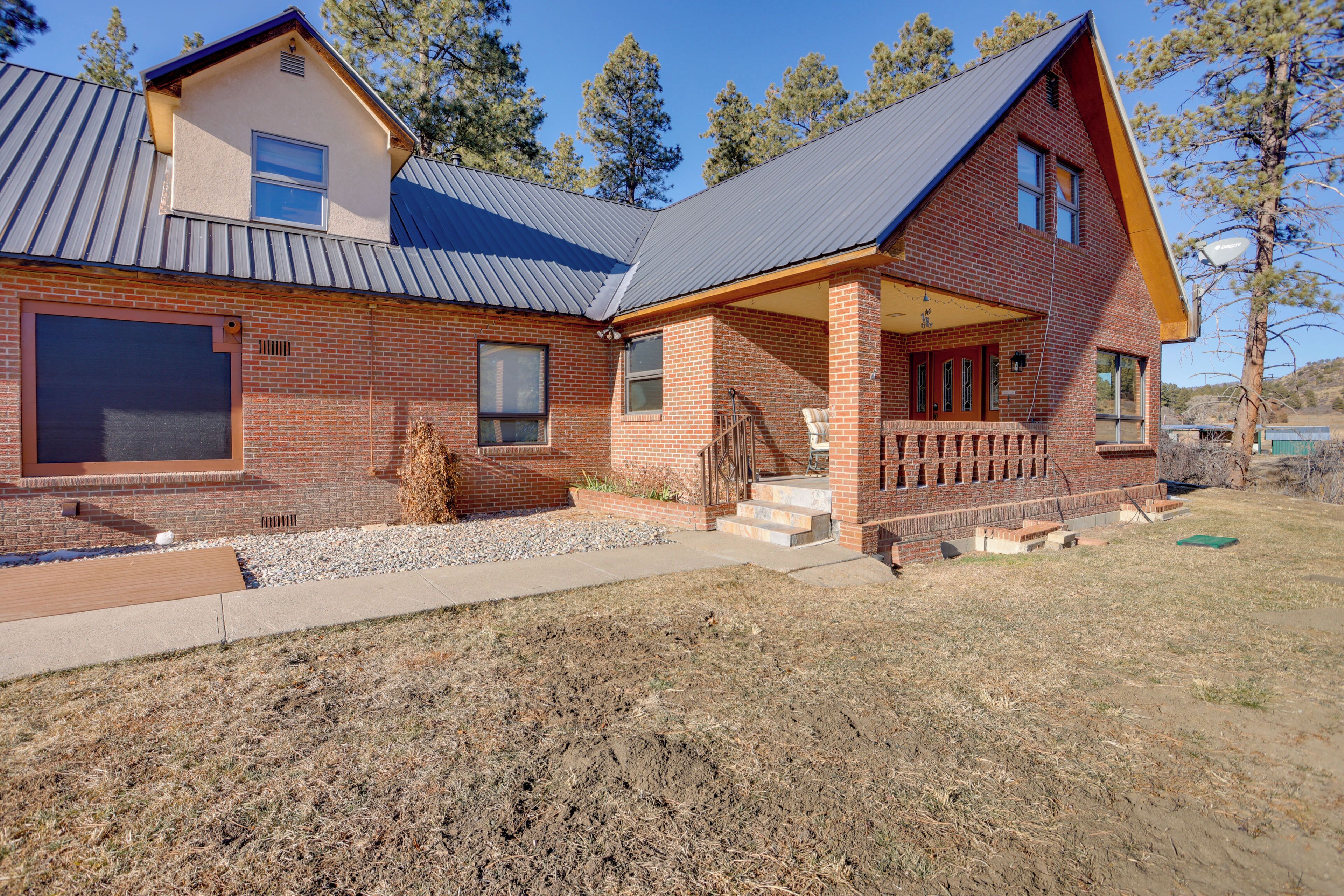 A two-story brick house with a large garage door, a covered porch, and a sloped metal roof.