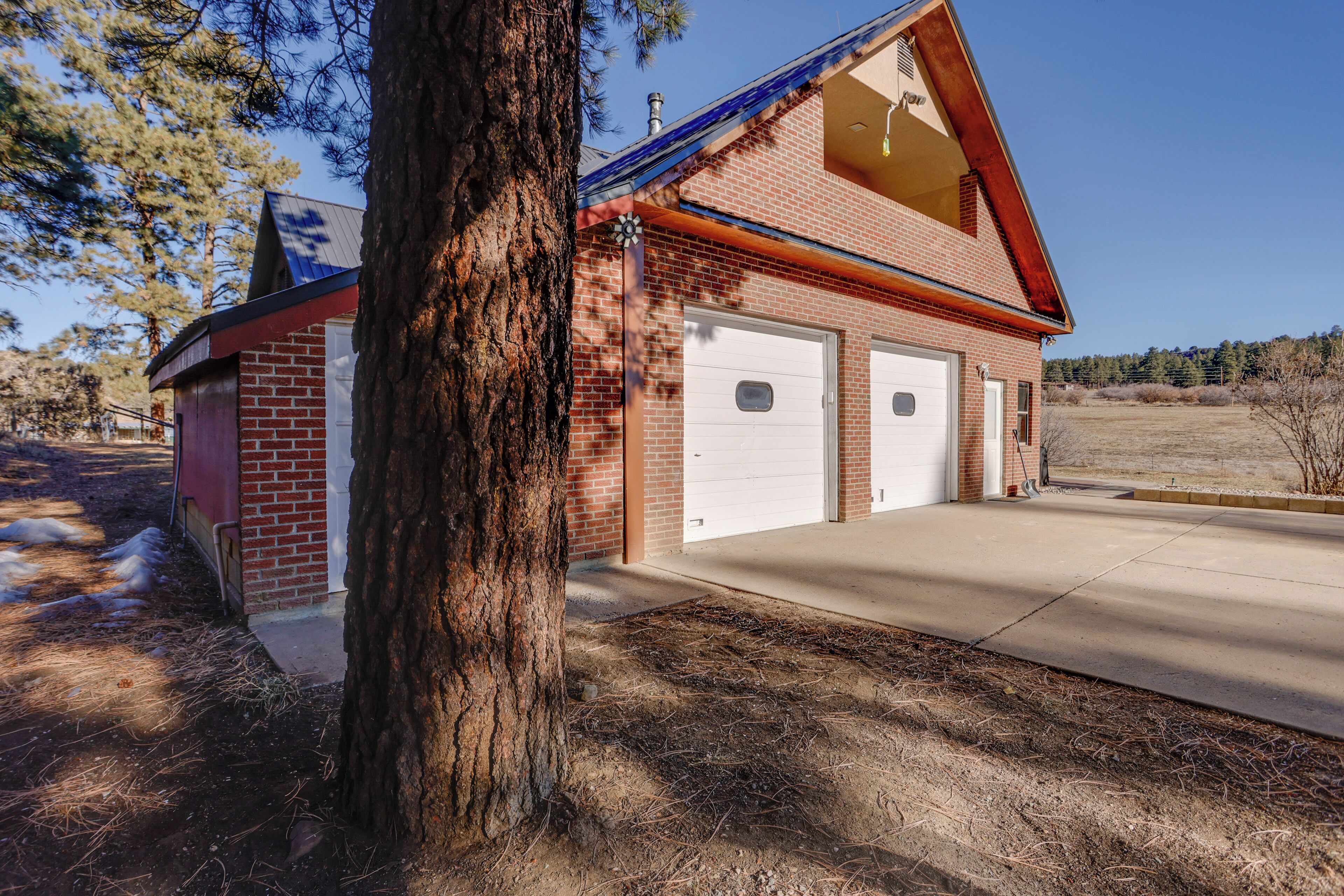 A two-story building with a brick facade, two garage doors, and a large tree in the foreground.