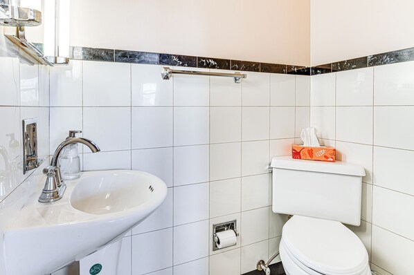 A bathroom with a white sink, a toilet, and a shower area. - Mid-century Stone Ranch In Central Columbus (Columbus)