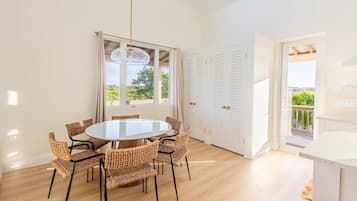 A bright room with a round table and wicker chairs, a large window, and a view of greenery outside.