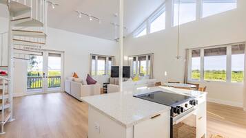 A spacious living area with a kitchen island, a staircase, and large windows offering a view of the outdoors.
