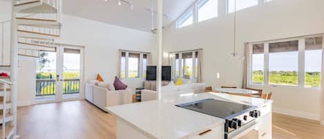 A spacious living area with a kitchen island, a staircase, and large windows offering a view of the outdoors.