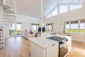 A spacious living area with a kitchen island, a staircase, and large windows offering a view of the outdoors. - Starlight Serenity - Hideaway w Stunning Views (Summerland Key)