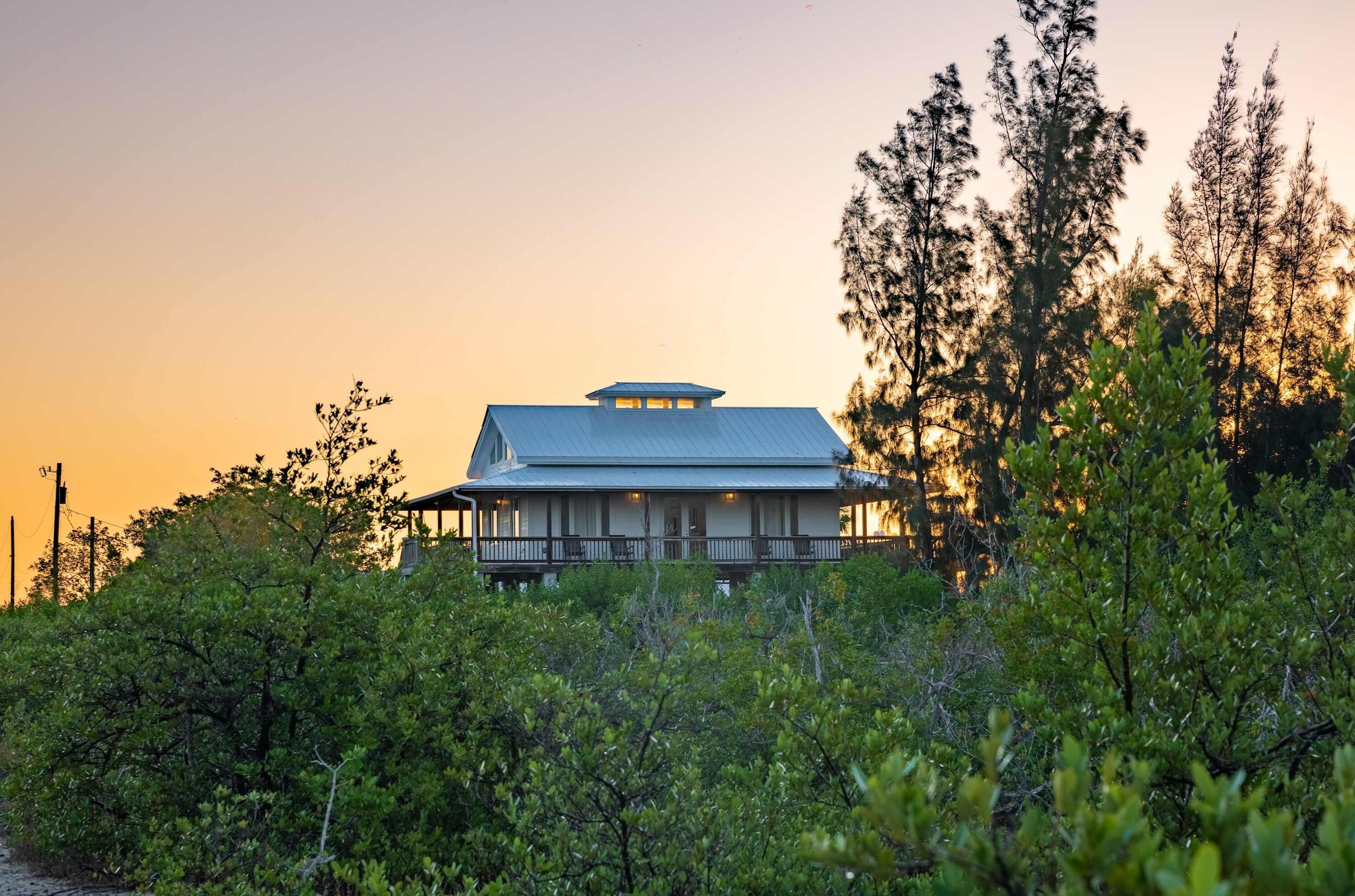 A house with a large porch and a covered upper level, surrounded by dense greenery and tall trees.
