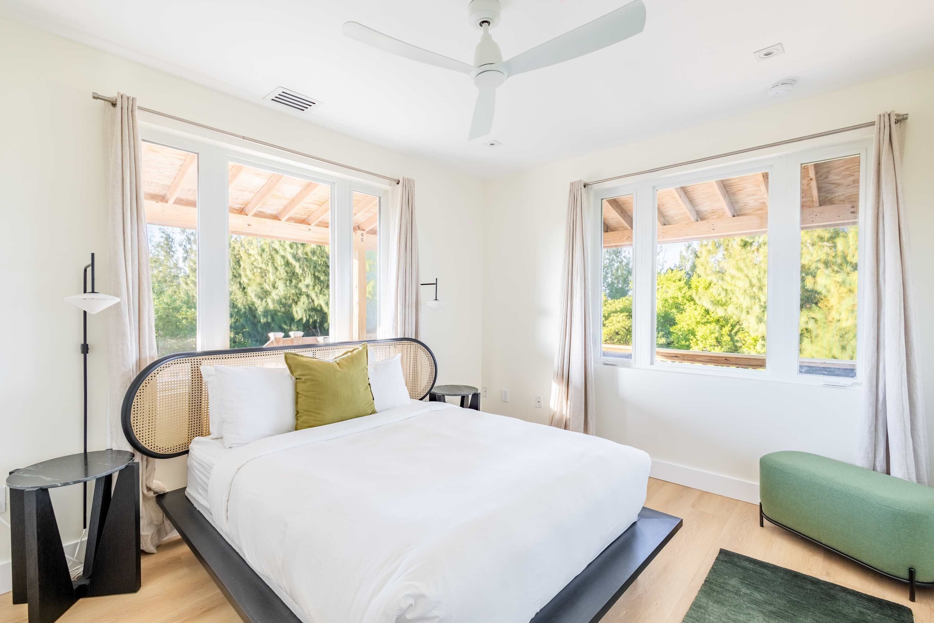 A modern bedroom with a large bed, two windows, a ceiling fan, and a green bench.