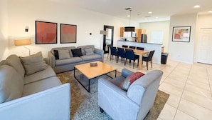 A modern living room with a grey sofa, a coffee table, and a dining area with chairs and a table. - Upstay Spacious 3BR Home w Resort Access (Kissimmee)