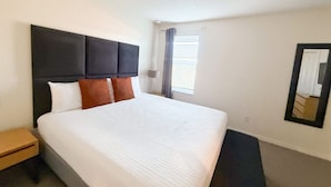 A hotel room with a large bed, a nightstand, a mirror, and a window with blinds. - Upstay Spacious 3BR Home w Resort Access (Kissimmee)