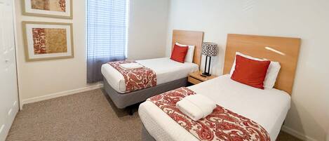 A hotel room with two beds, each with a red and white patterned bedspread, a wooden headboard, and a nightstand with a lamp.