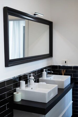 Un baño moderno con dos lavamanos blancos, un salpicadero de azulejos negros y un espejo grande sobre los lavamanos.