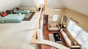 A loft-style bedroom with a sloped ceiling, a small seating area with a sofa and a coffee table, and a window with blinds. - Cozy pet-friendly cottage near Lake Michigan (Grand Beach)