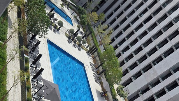 Un hotel moderno con una amplia piscina rectangular rodeada de sillones de descanso y sombrillas.