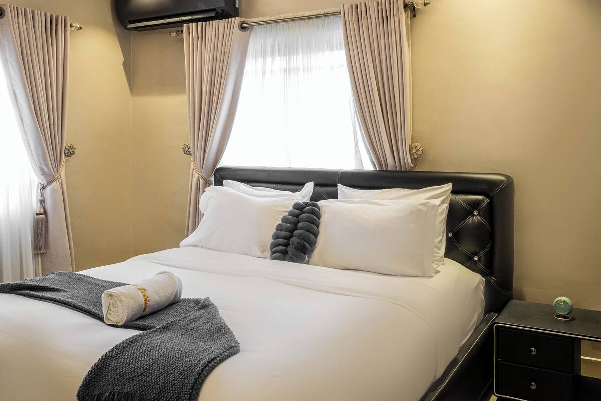 A modern bedroom with a large bed, a nightstand, and an air conditioning unit on the wall.