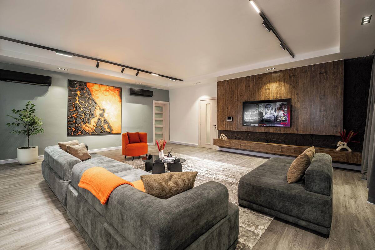 A modern living room with grey sofas, a large abstract painting, a flat-screen TV, and a wooden accent wall.