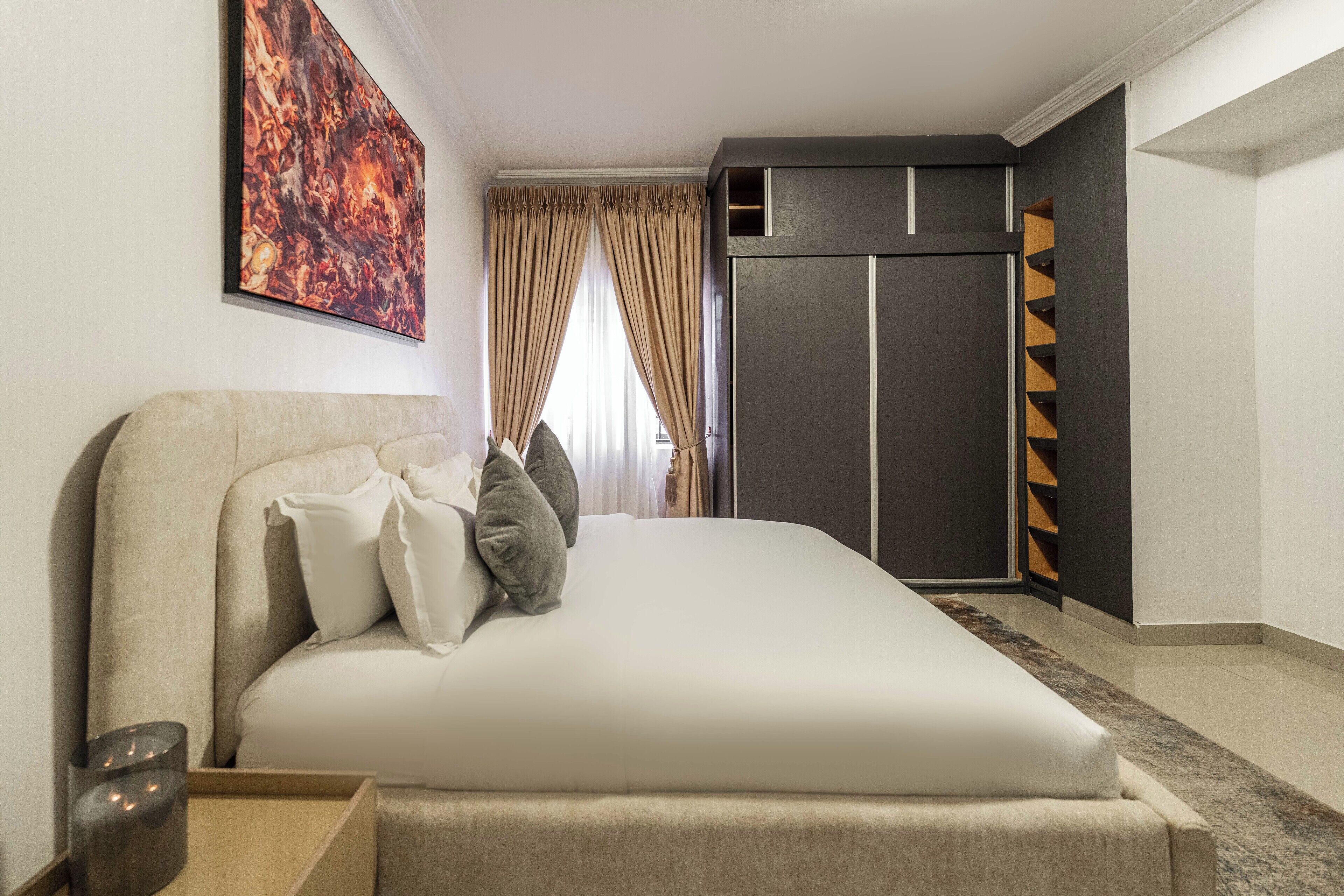 A modern hotel room with a large bed, a wardrobe, and a painting on the wall.