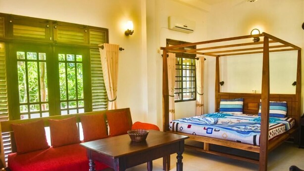 Une chambre avec un lit à baldaquin, un canapé rouge, une table en bois et une fenêtre avec des volets verts.