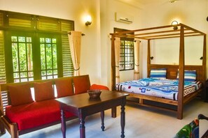 A room with a four-poster bed, a red sofa, a wooden table, and a window with green shutters. - Ravi Villa (Hikkaduwa)
