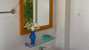 Une salle de bain avec un lavabo blanc, un vase bleu rempli de fleurs et un miroir avec un cadre en bois.