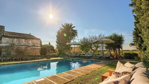 A swimming pool with lounge chairs and umbrellas, surrounded by greenery and a stone building. - Finca Son Valls (Felanitx)