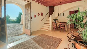 A rustic interior with a wooden staircase, a dining area with chairs and a table, and a large potted plant. - Finca Son Valls (Felanitx)