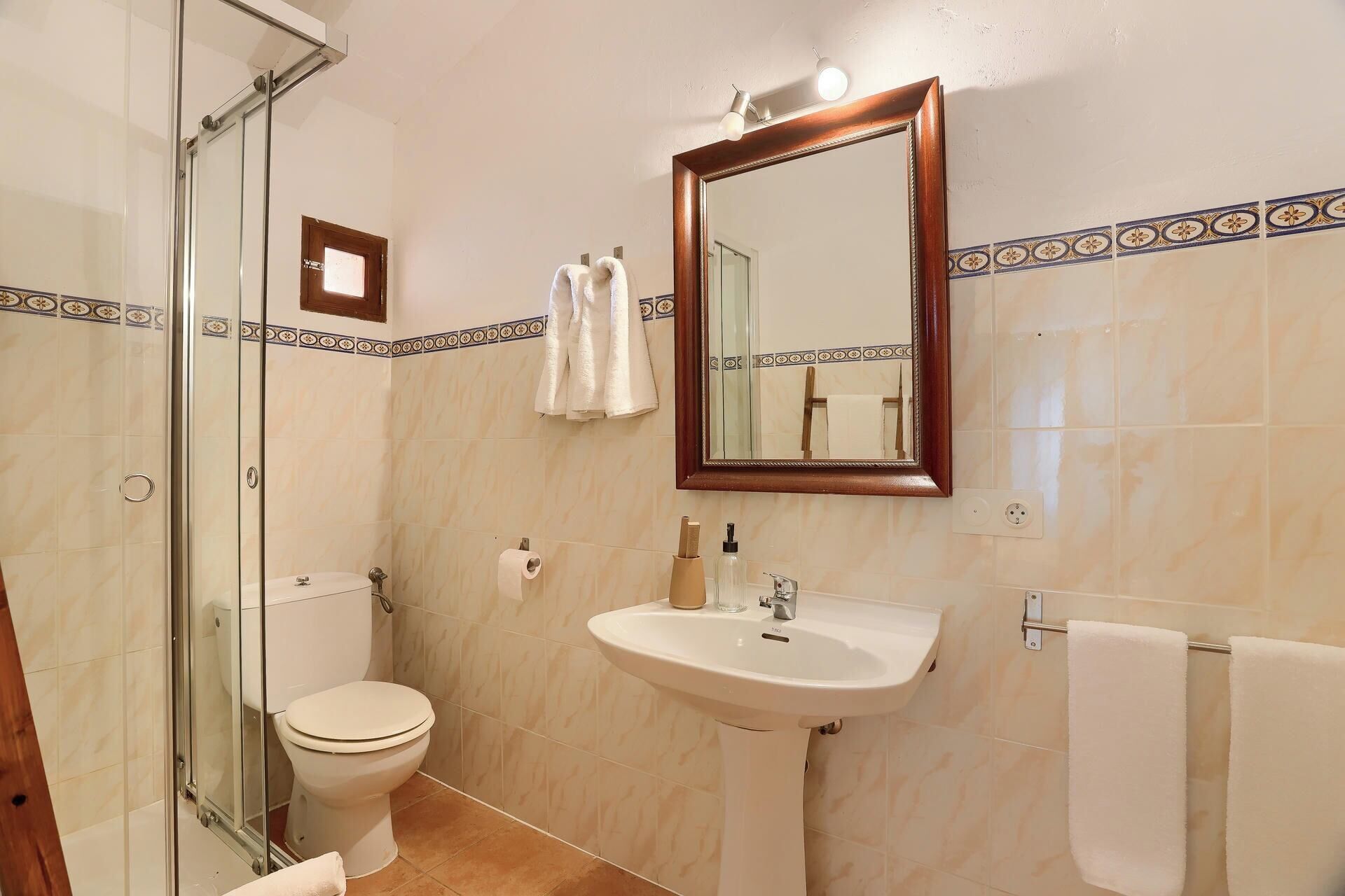 A bathroom with a glass shower enclosure, a toilet, a sink with a mirror above it, and a towel rack.