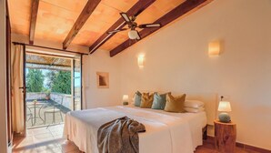 A bedroom with a large bed, a ceiling fan, a small table with a lamp, and a view of the outdoors through a glass door. - Finca Son Valls (Felanitx)