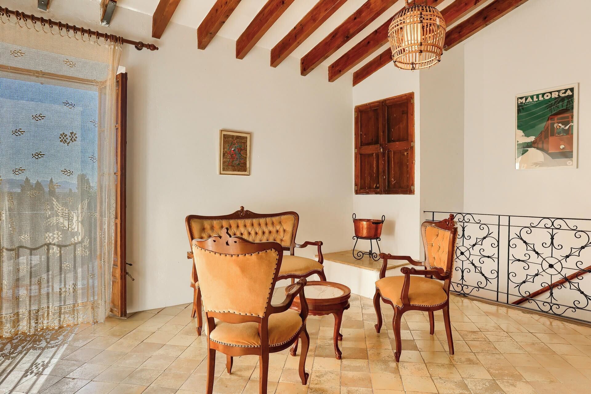 A room with a bed, two chairs, a small table, a hanging light fixture, a window with wooden shutters, and a poster on the wall.