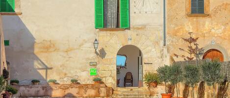 A building with a stone facade, green shutters, and a visible door labeled "AG."