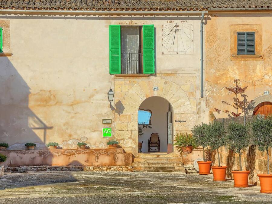 Un edificio con fachada de piedra, contraventanas verdes y una puerta visible con la etiqueta