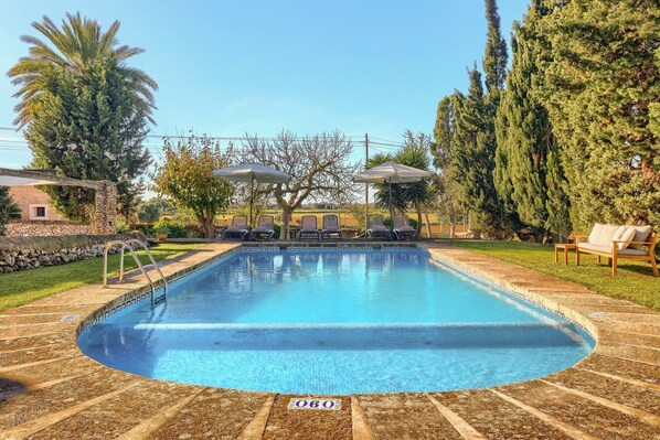 A swimming pool with lounge chairs and umbrellas, surrounded by trees and a stone wall. - Finca Son Valls (Felanitx)