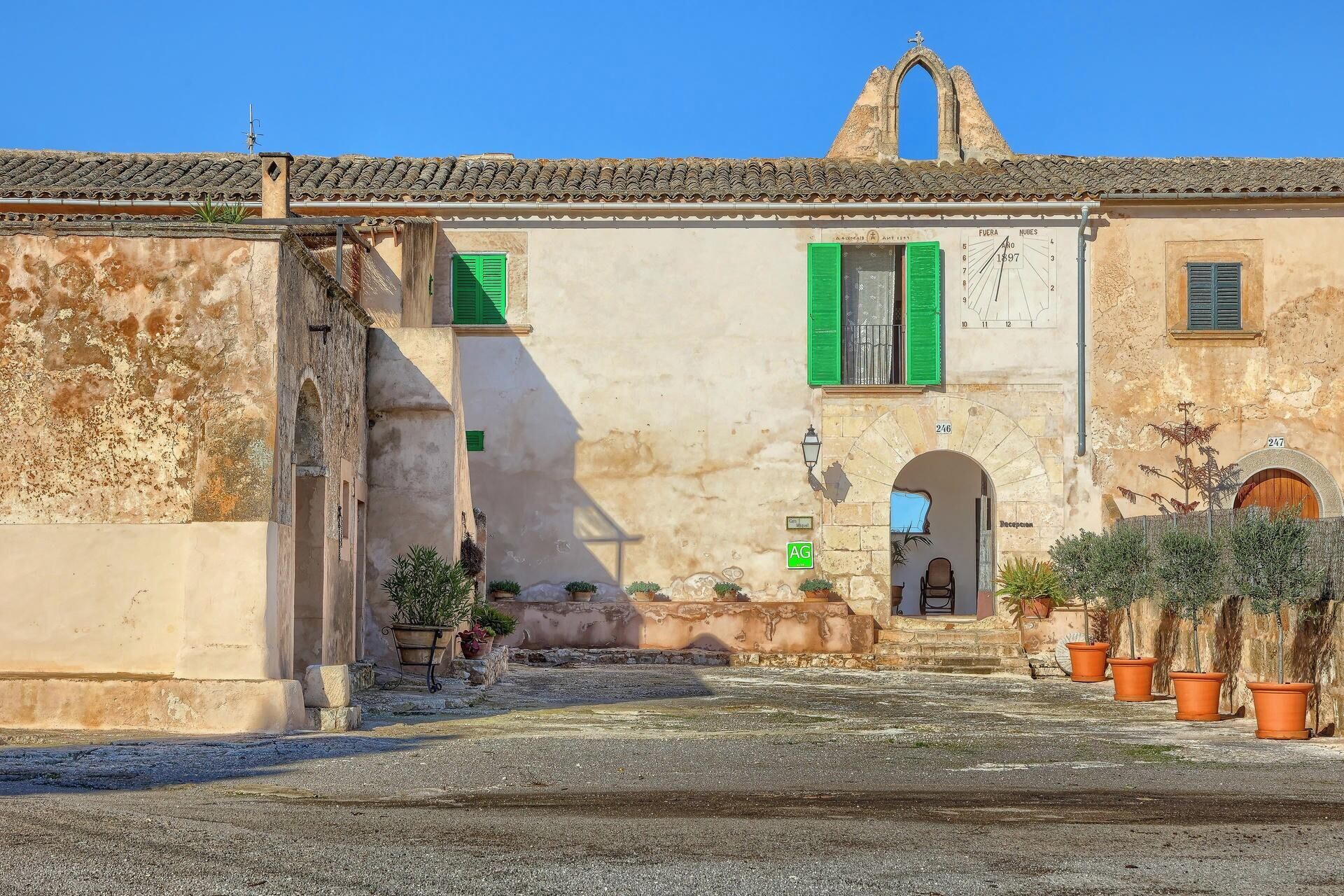 Edificio histórico con fachada desgastada, contraventanas verdes y una pequeña zona de recepción.