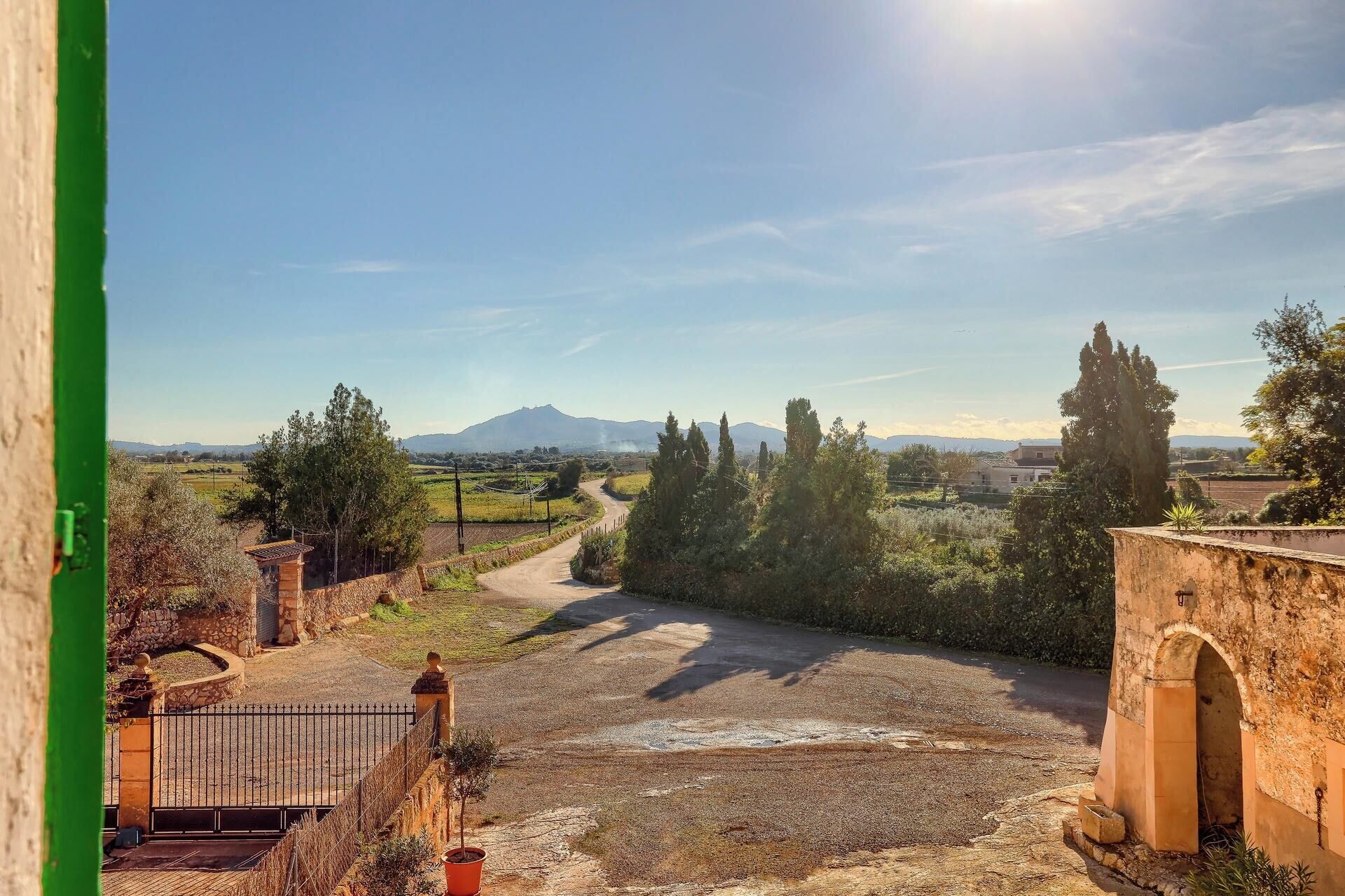 Un paisaje rural con un sendero de tierra que lleva a un edificio de piedra, rodeado de árboles y campos.