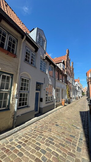Una calle empedrada flanqueada por edificios históricos con arquitectura europea tradicional, que incluyen tejados a dos aguas y fachadas de ladrillo.