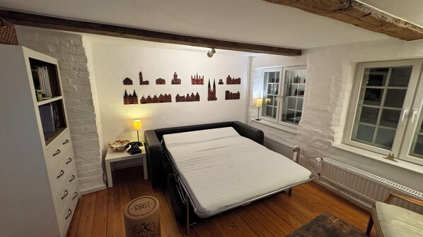 A bedroom with a bed, a nightstand, a lamp, a bookshelf, and a wall with a cityscape mural. - Beautiful vacation home with garden in the old town and private parking space (Lübeck)