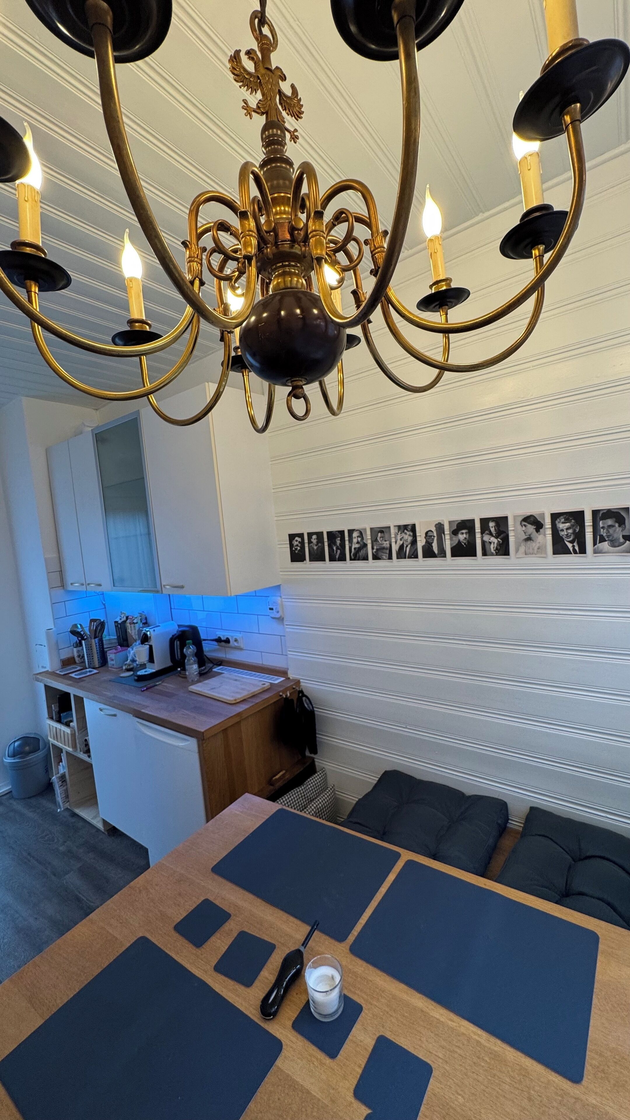 Un espace repas agrémenté d’un lustre, d’un mur recouvert de photographies et d’une cuisine en arrière-plan.