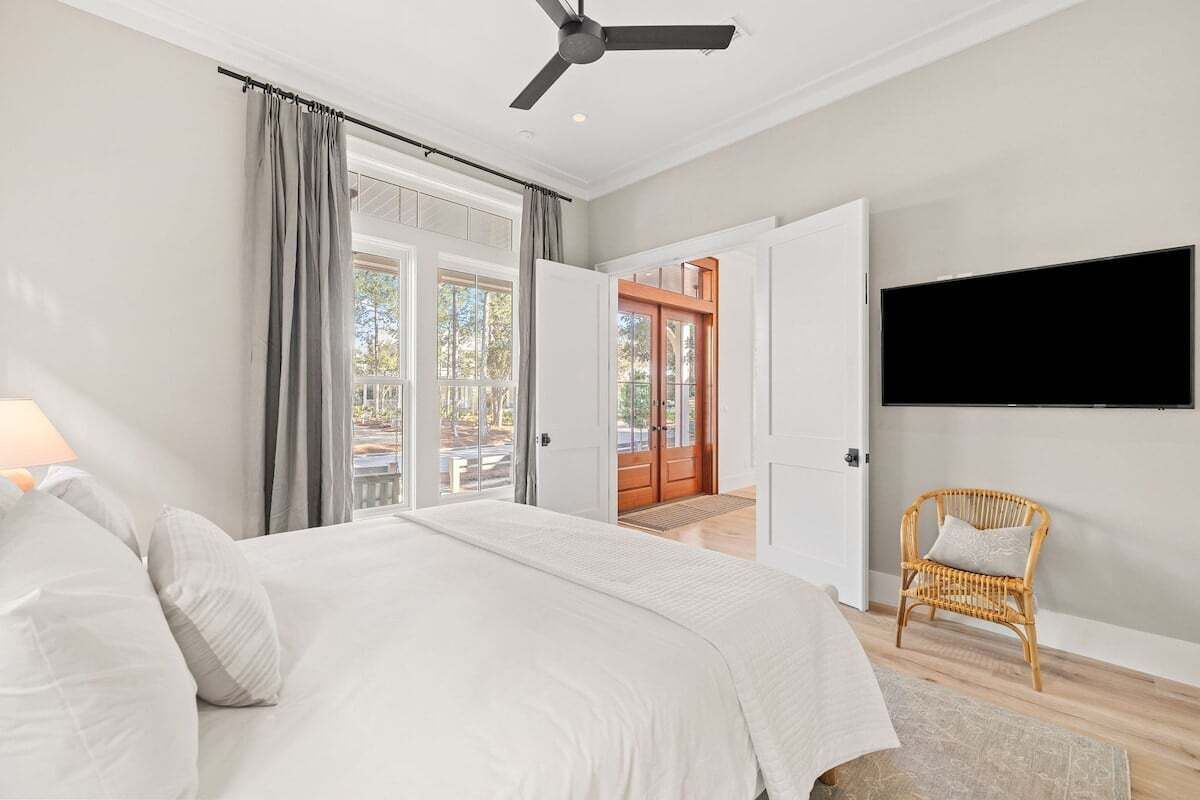 Un dormitorio con cama, ventilador de techo, televisor montado en la pared y una silla de mimbre.