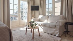 A living room with a beige sofa, a small round table with a plant, and a TV mounted on the wall.