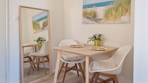 A dining area with a wooden table, white chairs, and a painting of a beach scene.