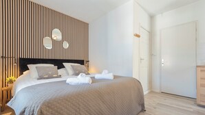 Ein aufgeräumtes Schlafzimmer mit einem großen Bett, einer Wand aus Holzlamellen und einer weißen Tür.