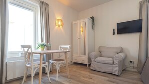 Ein Zimmer mit Esstisch und Stühlen, einem Sofa, einem Kleiderschrank und einem an der Wand befestigten Fernseher.