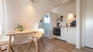 Una cocina moderna con armarios blancos, encimera de madera y horno empotrado. Hay una zona de comedor con una mesa y sillas, y una alfombra pequeña en el suelo.