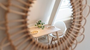 Un comedor con una mesa de madera, dos sillas, un florero con flores y un marco de espejo tejido.